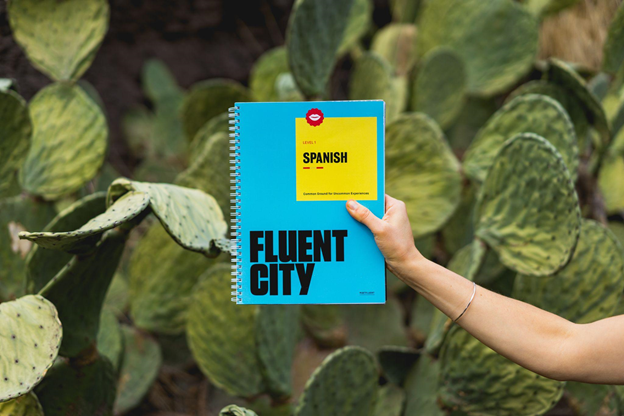 Get fluent in Spanish by immersing yourself in the language, a hand holding a book titled Fluent City