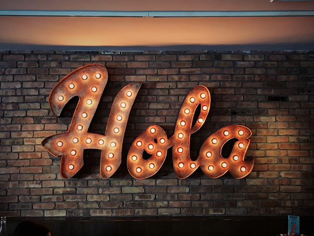 A neon sign over a brick wall saying Hola in Spanish