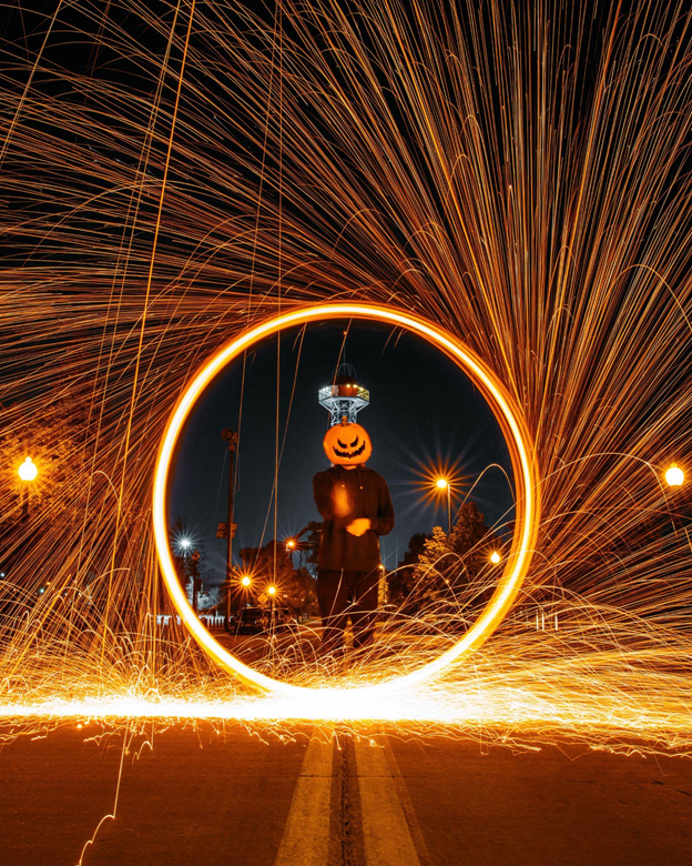 A Halloween celebration showing a man in a pumpkin mask standing in a flashy circle