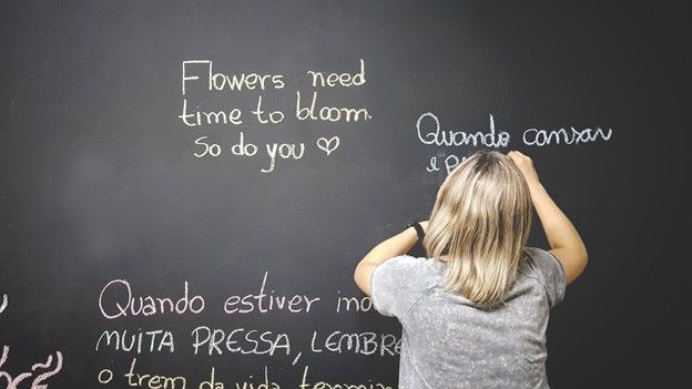 Teacher writing sentences in multiple languages on blackboard