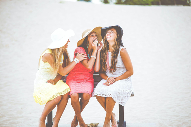 Three women sitting giggling while sharing funny language mistakes on the beach