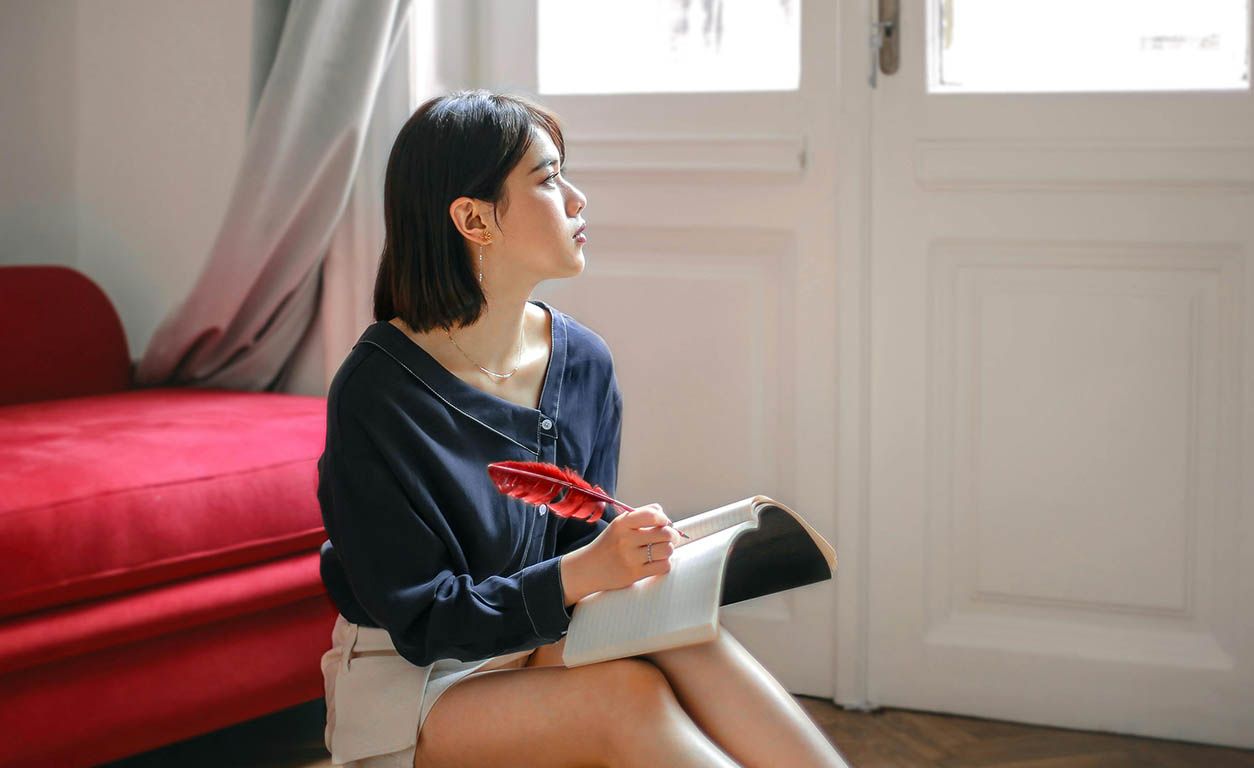 Woman thoughtfully writing in her notebook at home